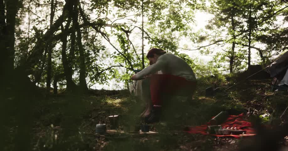 A man gives a woman a plate of food while they are camping outside in the woods and then she leans in to give him a small kiss on the cheek