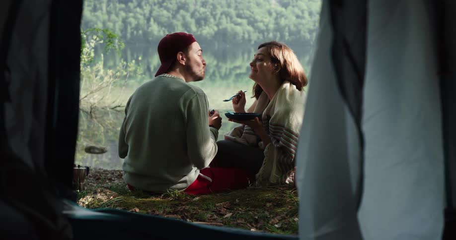 A couple kisses and plays as they eat a meal in front of a tent