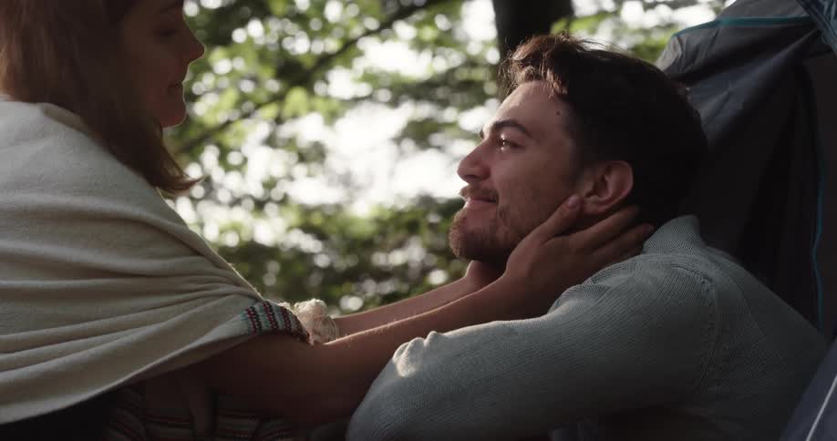 Young couple kissing on the entrance of a tent in the forest at morning