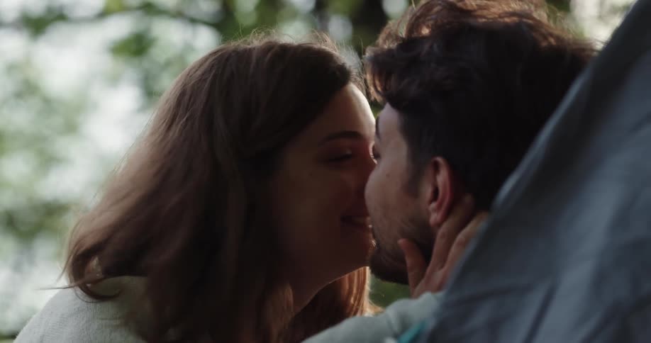A man is sitting back as a woman moves up to kiss him