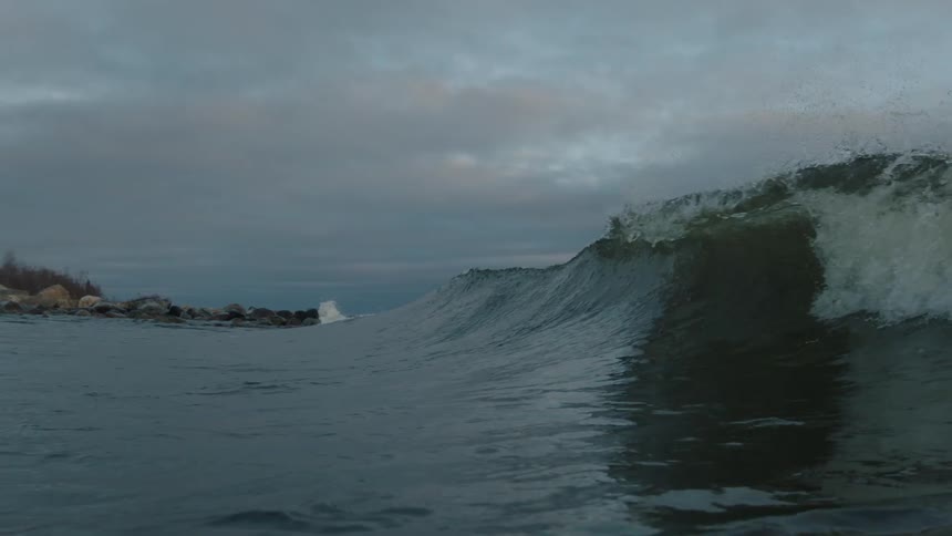 Waves roll under a cloudy sky near sunset