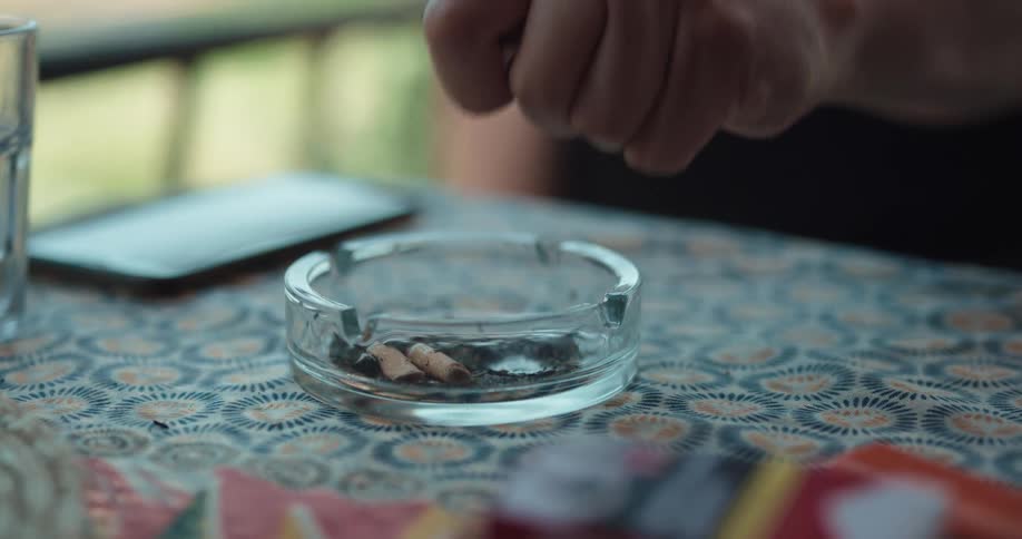 A person is sitting at a table and putting out a cigarette