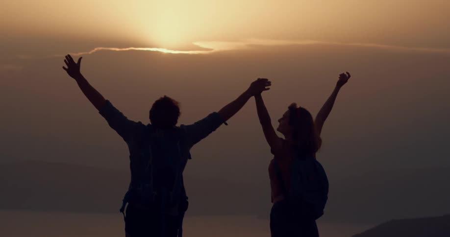 Couple raise clasped hand in celebration viewing fog shrouded water