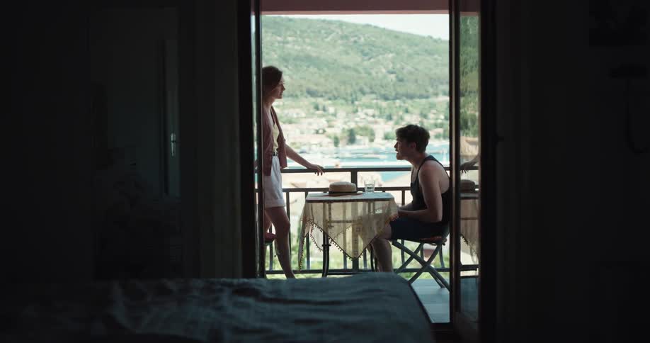 A woman and man argue on a balcony with a mountain scenery in the distance