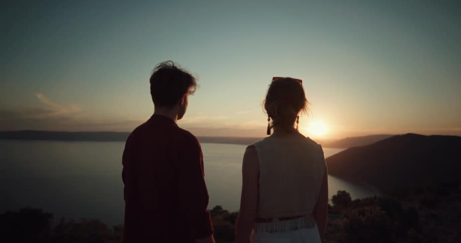 Man and woman standing on a mountain and watch the shore and sunset