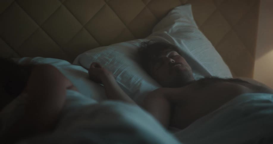 A man and woman lay sleeping in a bed with the light on
