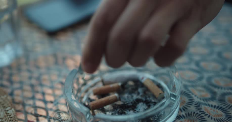 A man crushes a cigarette butt over an ashtray