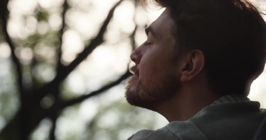 Man sits outdoors looks around and takes a deep breath before smiling and talking