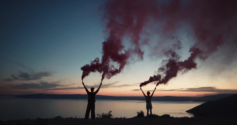 Two people are standing on the coast holding up items that smoke
