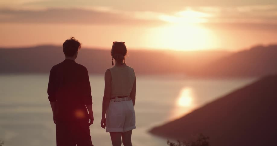 Two people standing by a lake at sunset