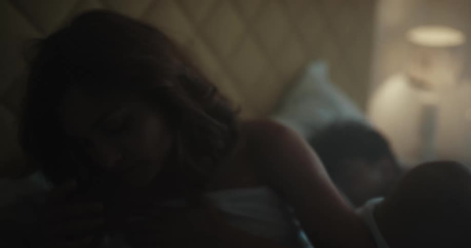 Young woman wakes up in bed next to her couple inside a dimly lit bedroom