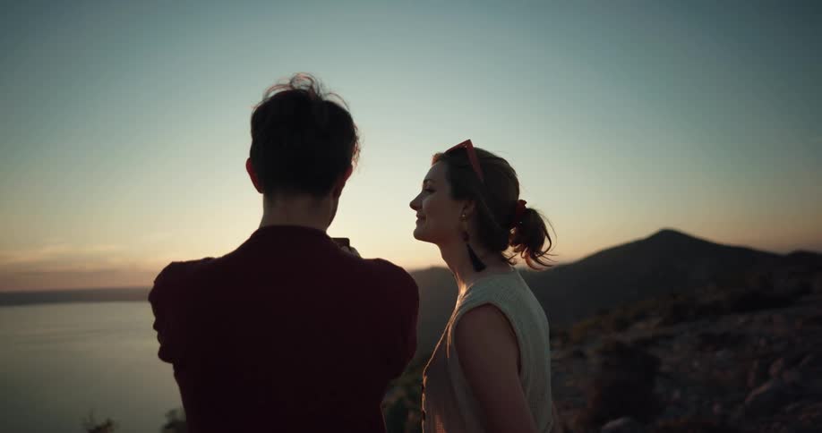 A man and woman are standing outdoors and watching the sunset