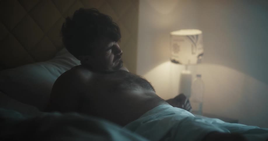A man rubs his face as he wakes then reaches over for a water bottle on the night stand