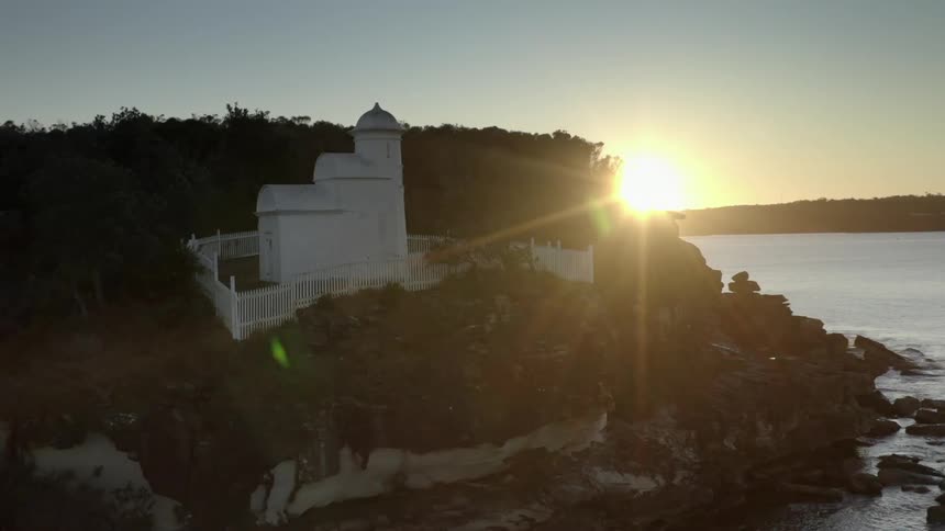 A white building surrounded by a white fence on a cliff overlooking the ocean during the day