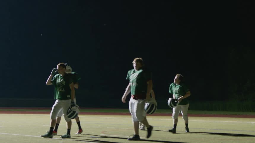 A group of football players take off their helmet and walk across a field