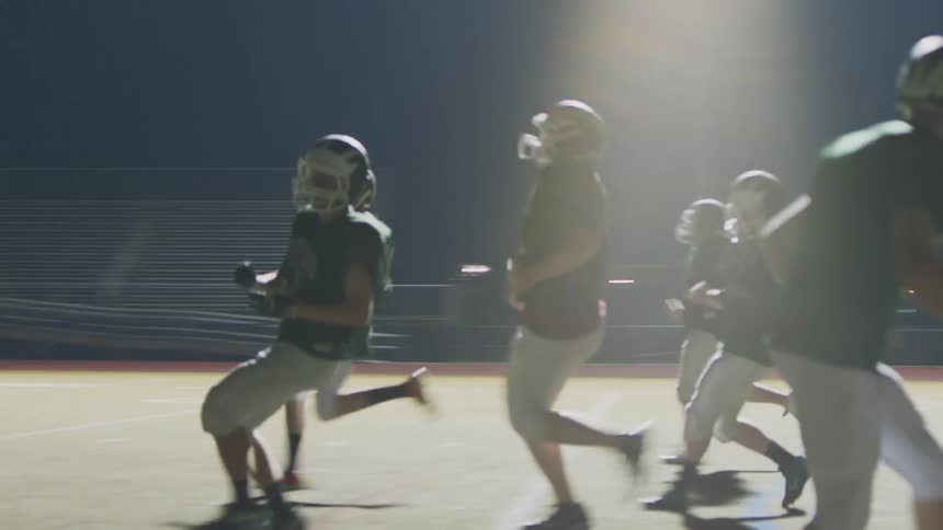 Football players in full gear running down a stadium field at night