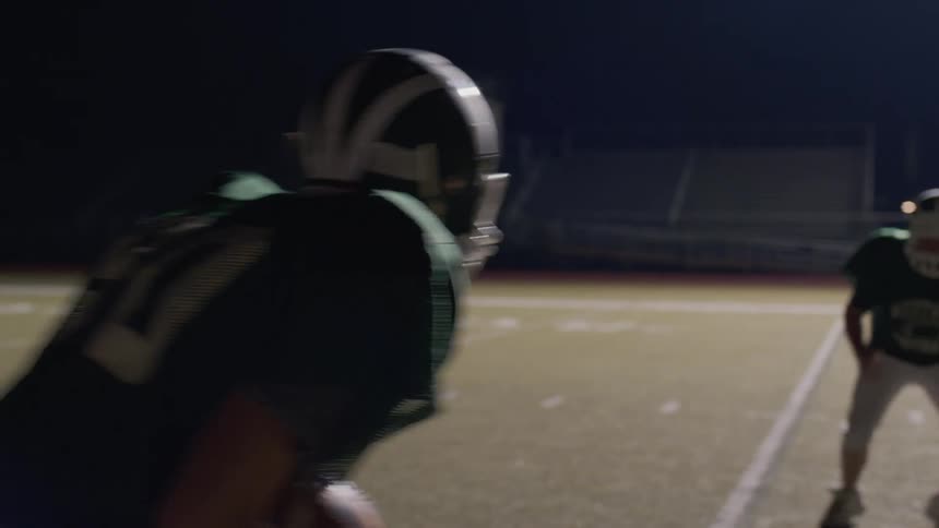 Football players practice on a field at night
