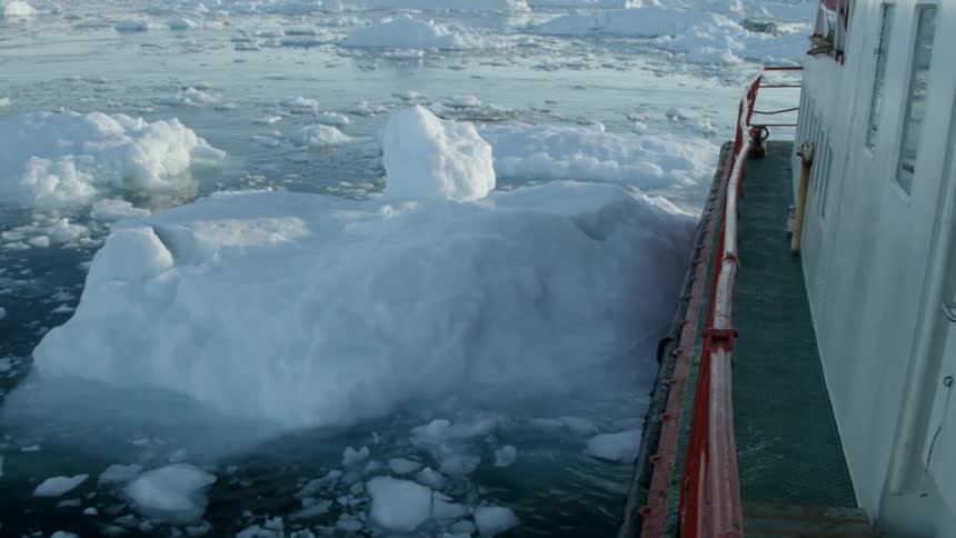 A boat sails knocking into a piece of ice in the water