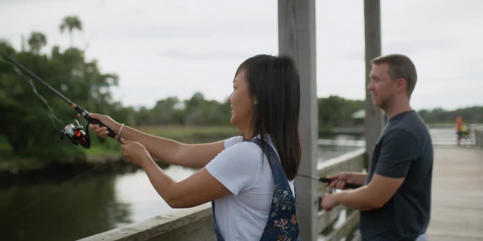 A woman casts from a dock as she fishes beside a man