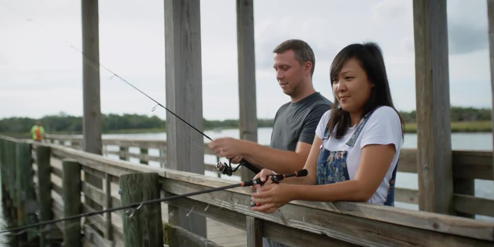 A man and woman stand on a dock and fish