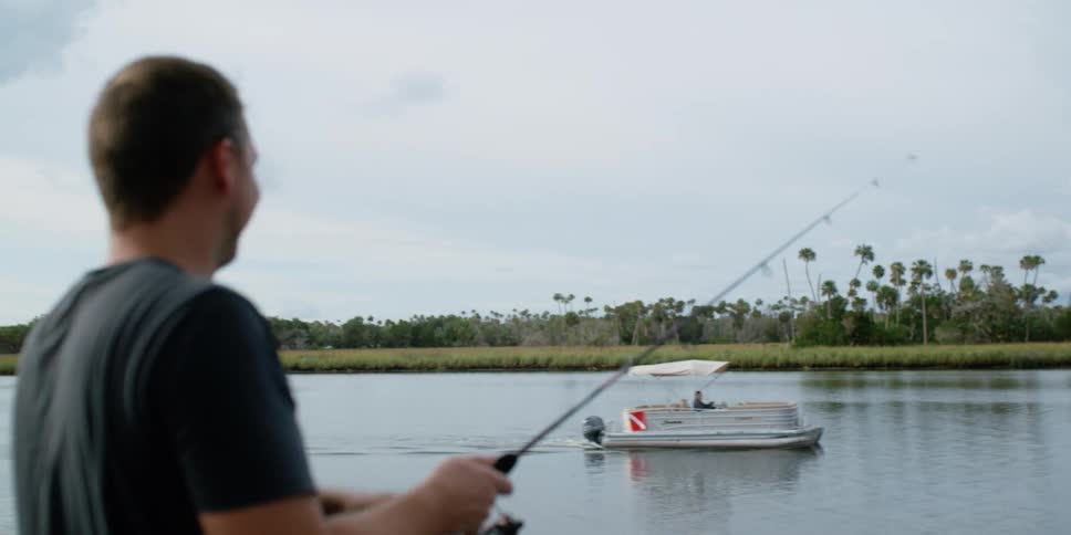 A man waves to a boat passing by as he is fishing