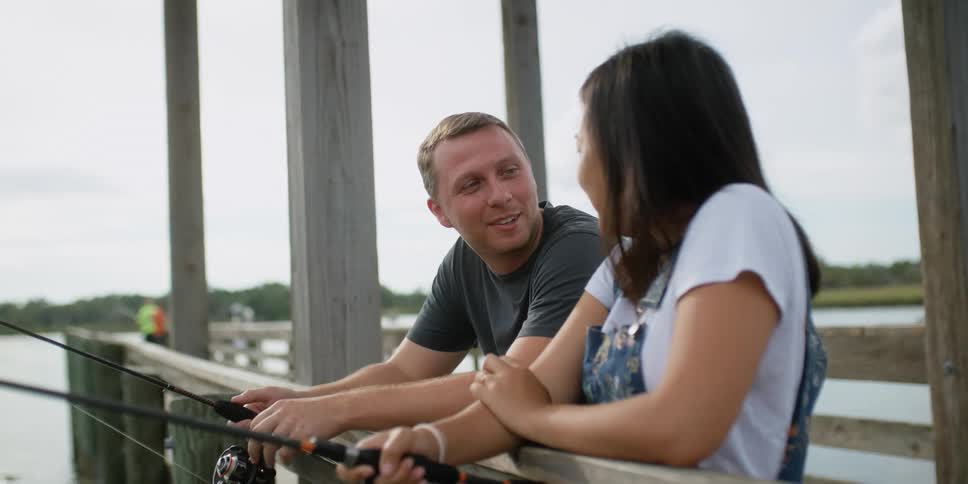 A man and woman stand on the dock and talk and laugh as they fish