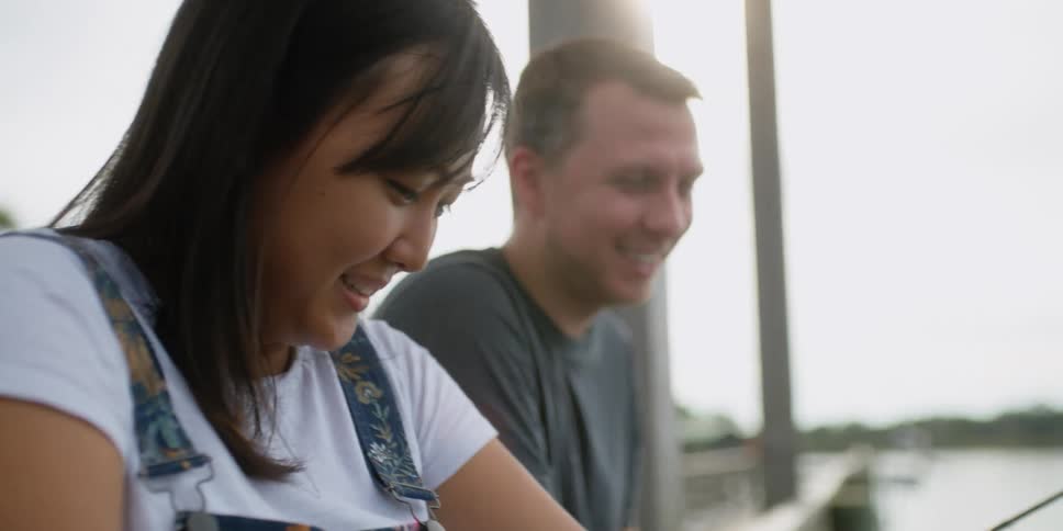 A man and woman laugh as they fish on the pier