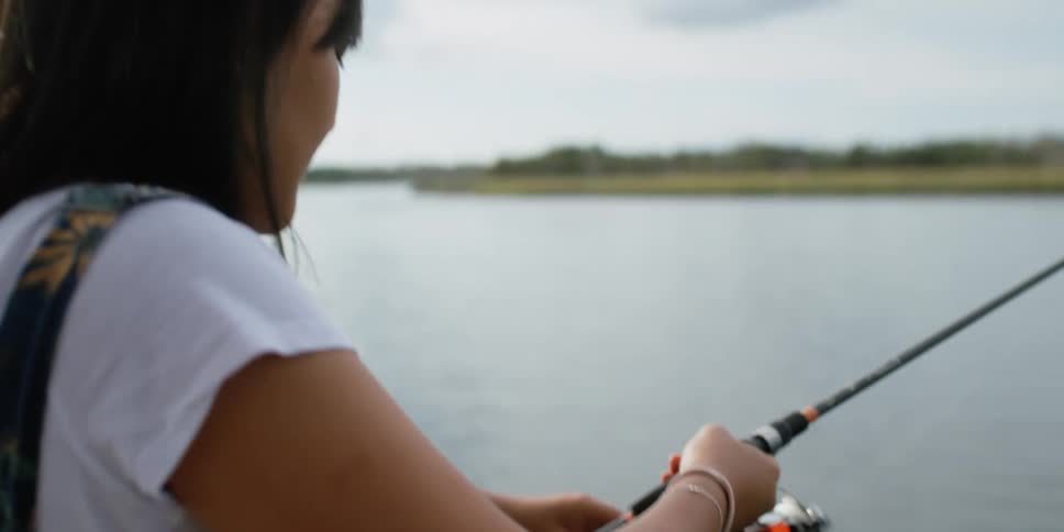 A woman stops looking across a lake to reel in a fish