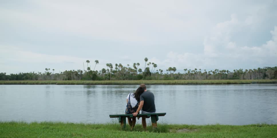 Man and woman hug as they sit on a bench overlooking the lake