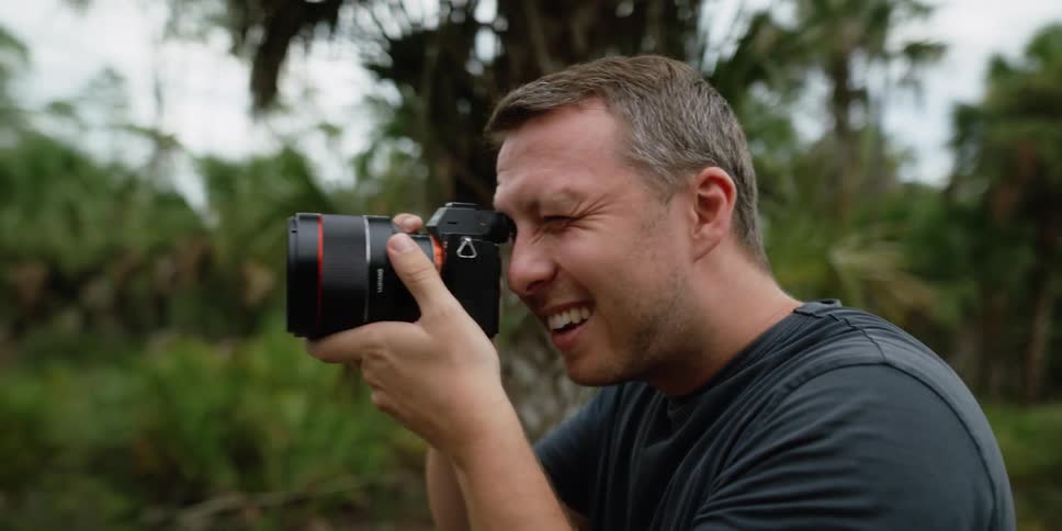 A man holds a camera up to his face taking pictures outside