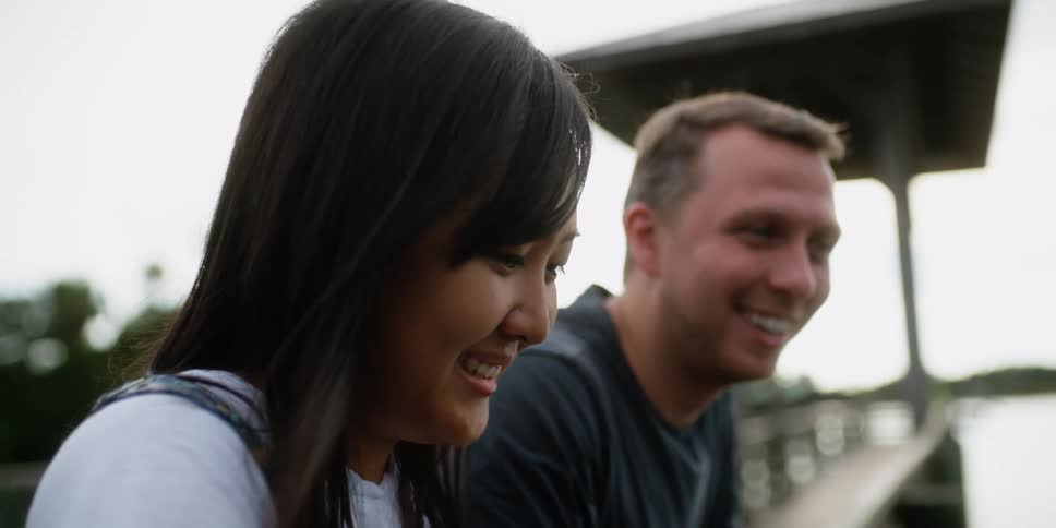 A man and woman are sitting on a dock and talking to each other