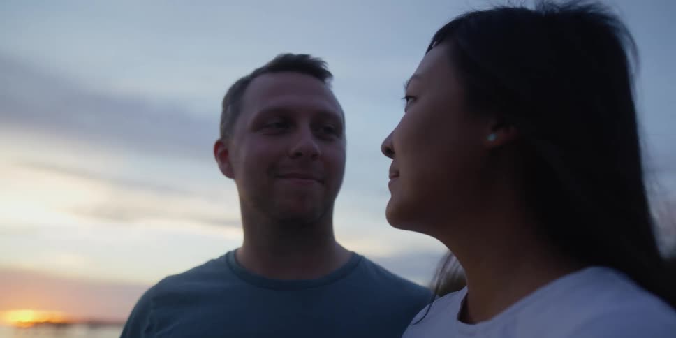 A man gazes at a woman lovingly and smiles at sunset