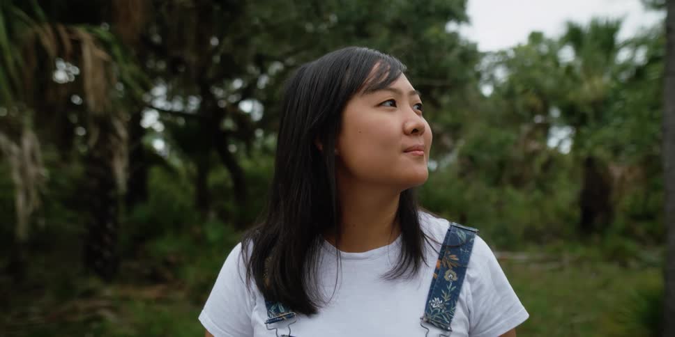Asian woman stands in a forest looking around thoughtfully