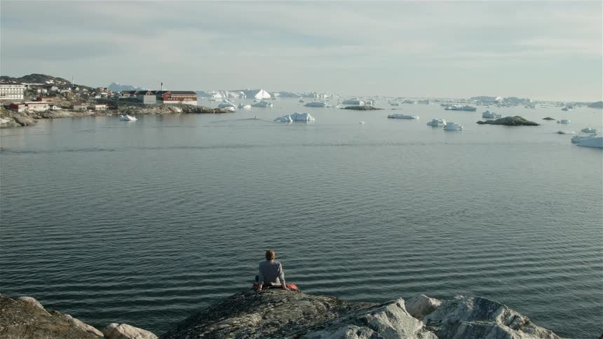 A person watches a body of water from a rock