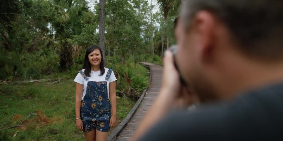 A woman smiles in front of a man taking a picture of her with a camera