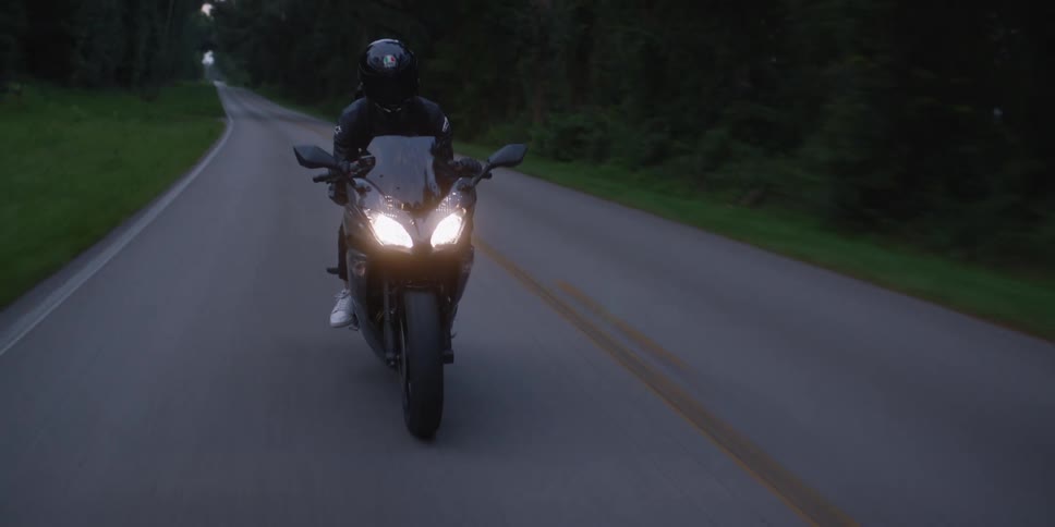 Cyclist wearing a black jacket and black helmet is riding a motorcycle with the headlights on