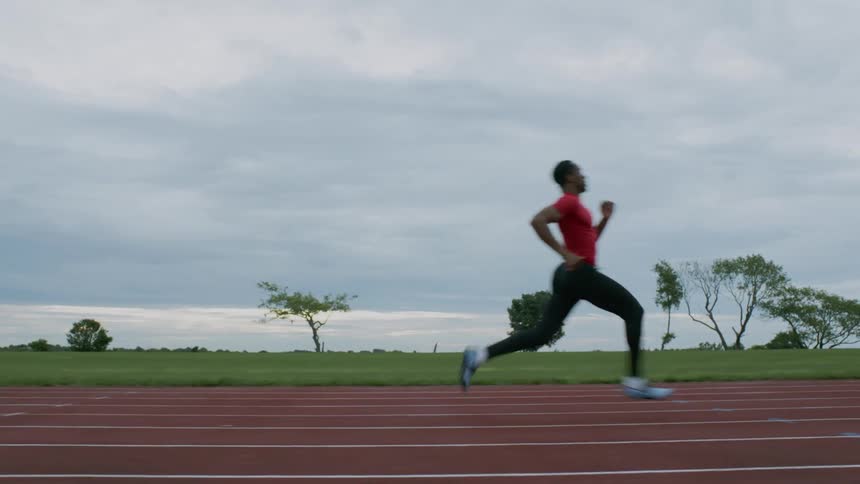 A runner is running down a track on a cloudy day