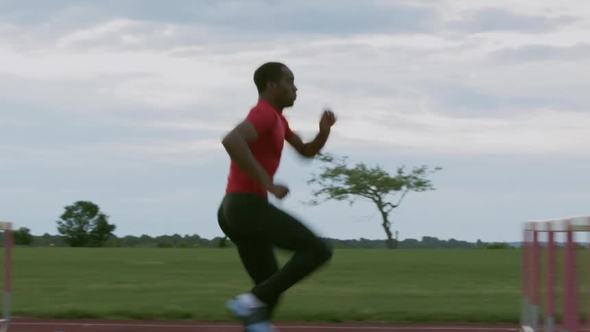 Man jumping hurdles on a running track outside on a cloudy day