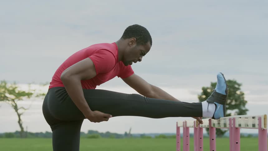 Man stretching his leg on a hurdle outside on a cloudy day
