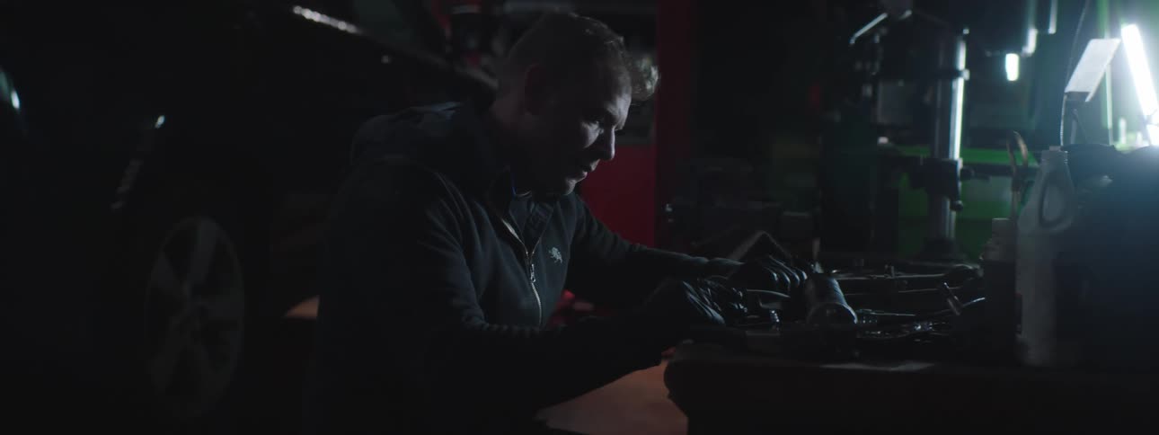 A man is working on a car in a garage at night