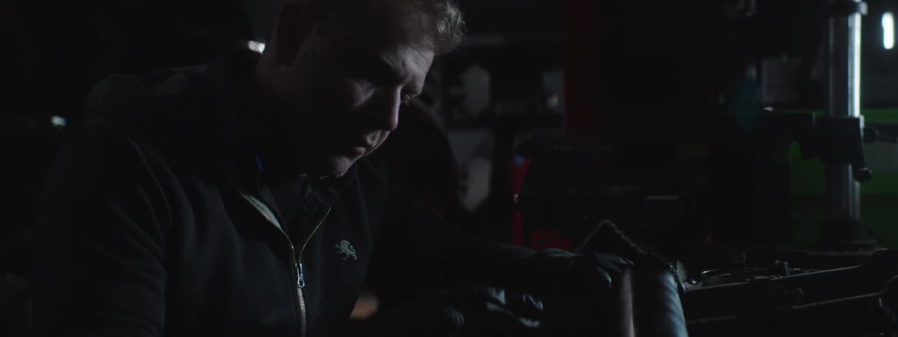 A man with gloves in a garage working with a vehicle and a wall in the background