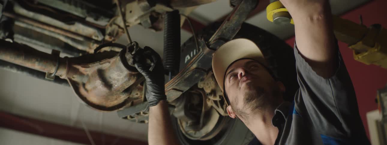 A man examines a car from underneath in a garage