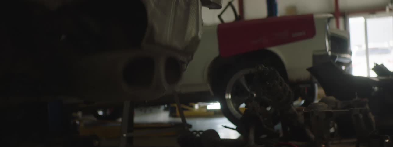 Two vehicles in a garage with parts with a wall and window in the background