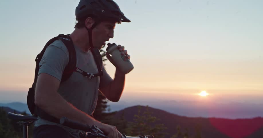 Cyclist drinks water after hard climb at the top of a mountain during sunset