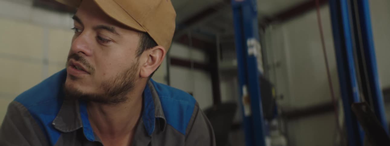 Man with a beard and wearing a cap talks and turns his head while in a workshop