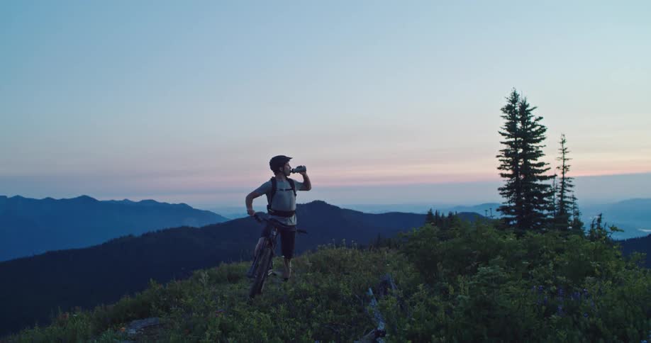 A man on a bike is drinking from his water bottle on top of mountain