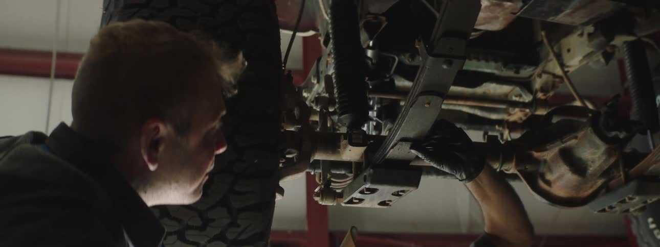 A mechanic looks underneath a vehicle that is lifted in the air at a commercial garage