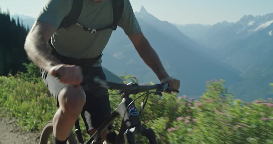 A man on a mountain climbs a trail with exposed mountain peaks in the background