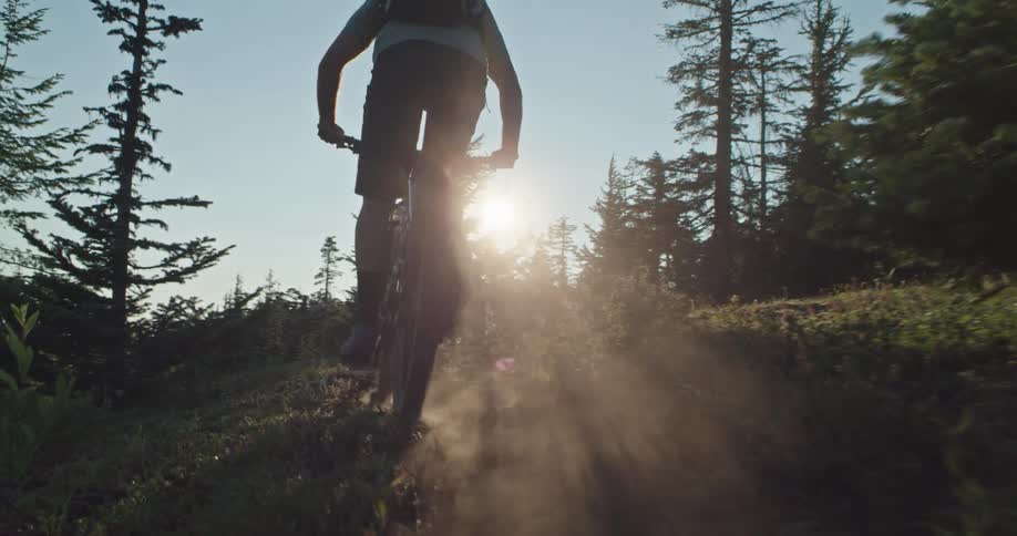 A mountain biker pedals through a dusty alpine trail at sunset