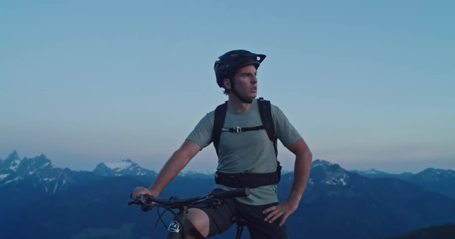 A man in a mountain ranges catches his breath as he rests on his bike